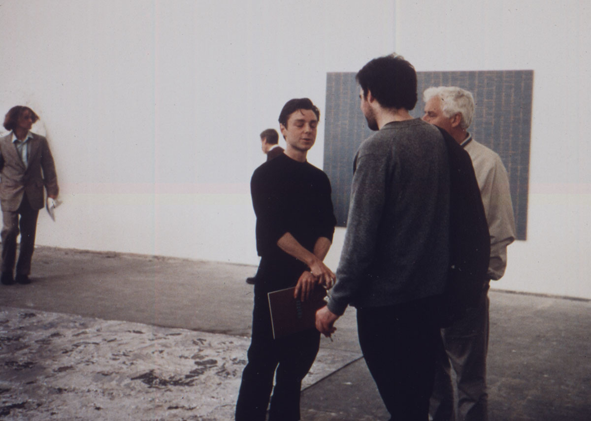 Opening night of “Freeze,” part 2, with (left to right) Richard Patterson, Miles Glenn, and Matt Patterson, and works by Angus Fairhurst on the wall. The lead and bronze floor piece is Anya Gallaccio’s Waterloo. As reproduced in Biennials and Beyond